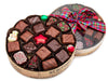 A round box with a clear lid tied with a festive holiday ribbon. The box contains 20 pieces of assorted chocolates including a white chocolate snowman and red foiled chocolate star.