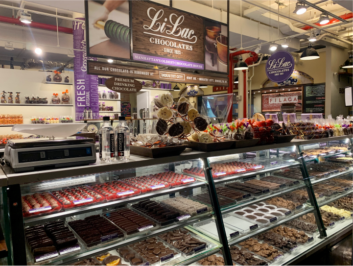 The front counter of a Lilac Chocolates store, wit a variety of chocolate treats on display inside the case and on top of the glass counter