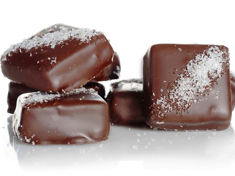 Caramel squares enrobed in milk and dark chocolate are stacked up together. The squares have a diagonal line of sea salt across the top.