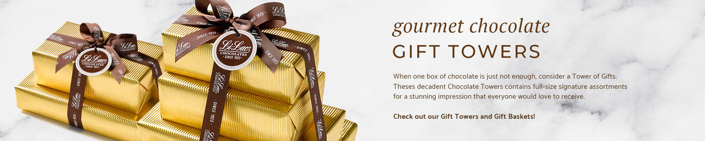a tower of two chocolate gifts wrapped in a handsome gold stripe paper and tied together with a brown lilac ribbon and hang tag, next to a tower of three gifts on a marble background.