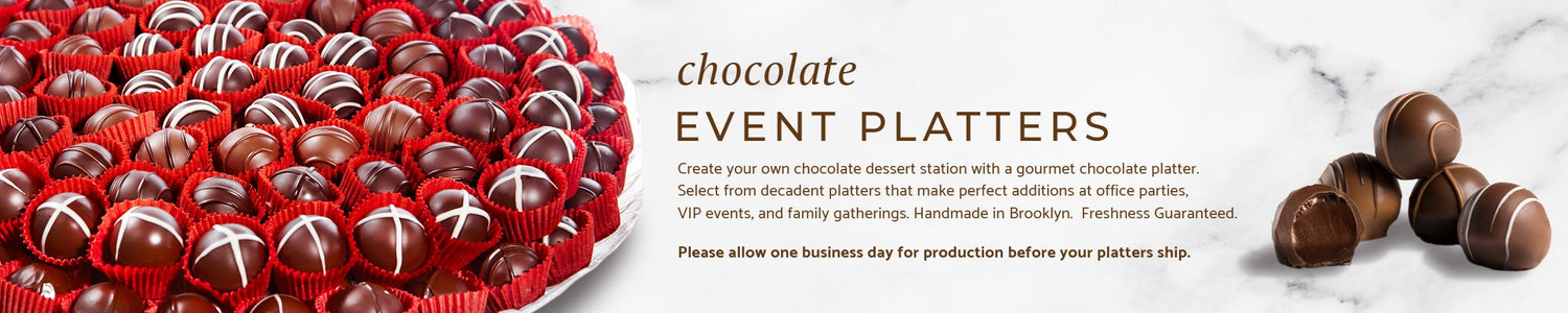 a large tray of truffles stacked two levels high on a marble background along with 5 truffles arranged on the opposite side with one truffle cut open showing the ganache inside.