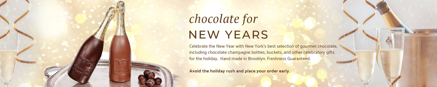 two chocolate champagne bottles on a sliver tray with truffles and a yellow bubbly background, along with a real champagne bottle, bucket and two glasses of champagne.