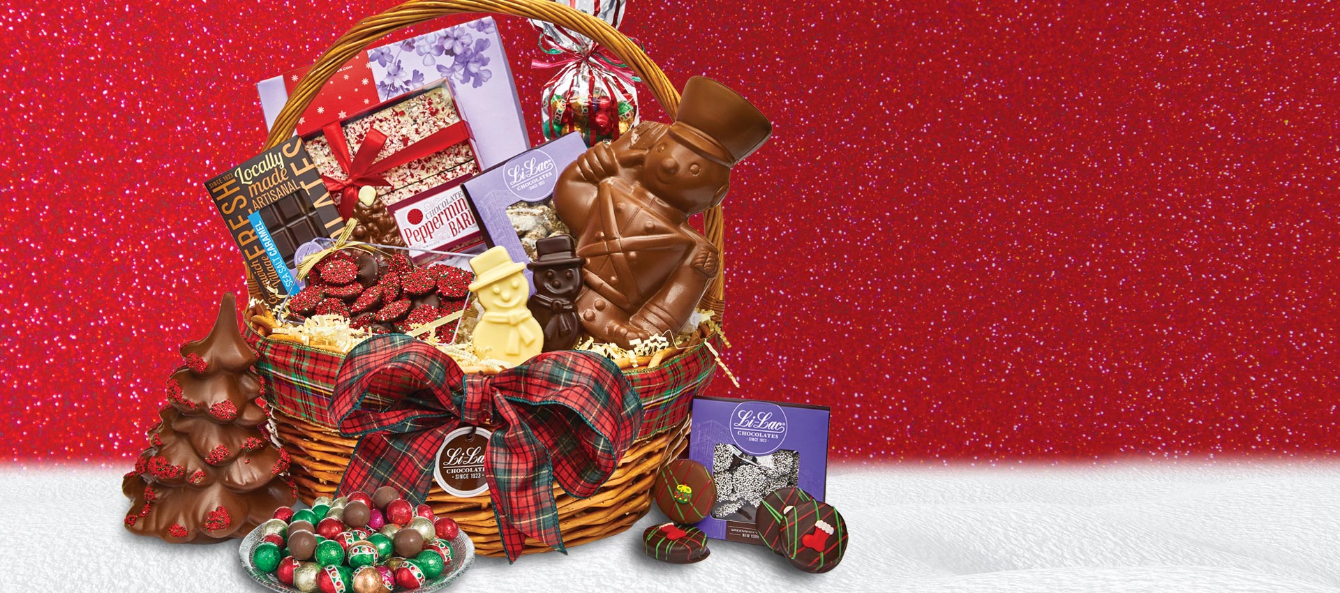 A festive basket filled with Christmas chocolates on a showy table and a red background.
