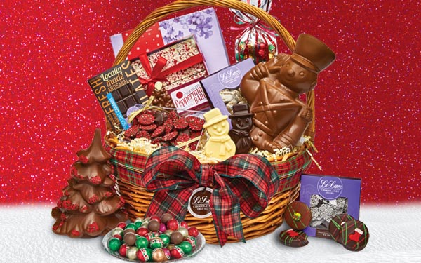 A large basket filled with Christmas chocolates sitting on a snowy blanket against a red background.