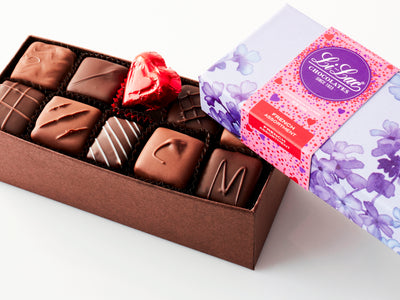 An open box showing the chocolate with a Valentine-motif box top partially covering the chocolates