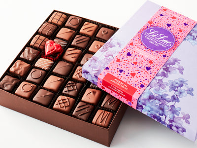 An open box showing the chocolate with a Valentine-motif box top partially covering the chocolates