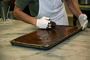 A tray of hazelnut chocolate being covered with chocolate by hand with a man wearing a white glove.
