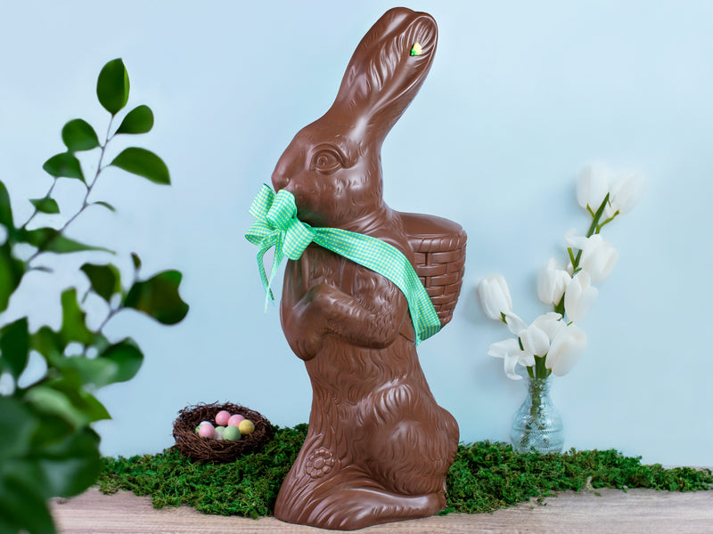 A very large chocolate bunny standing on a table with florals on a blue background.