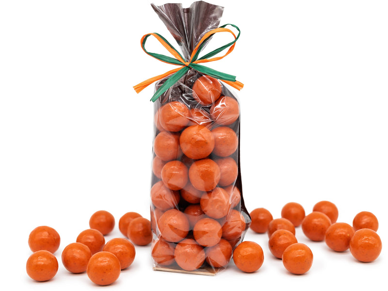 A clear bag of orange colored malt balls tied with a festive fall ribbon.