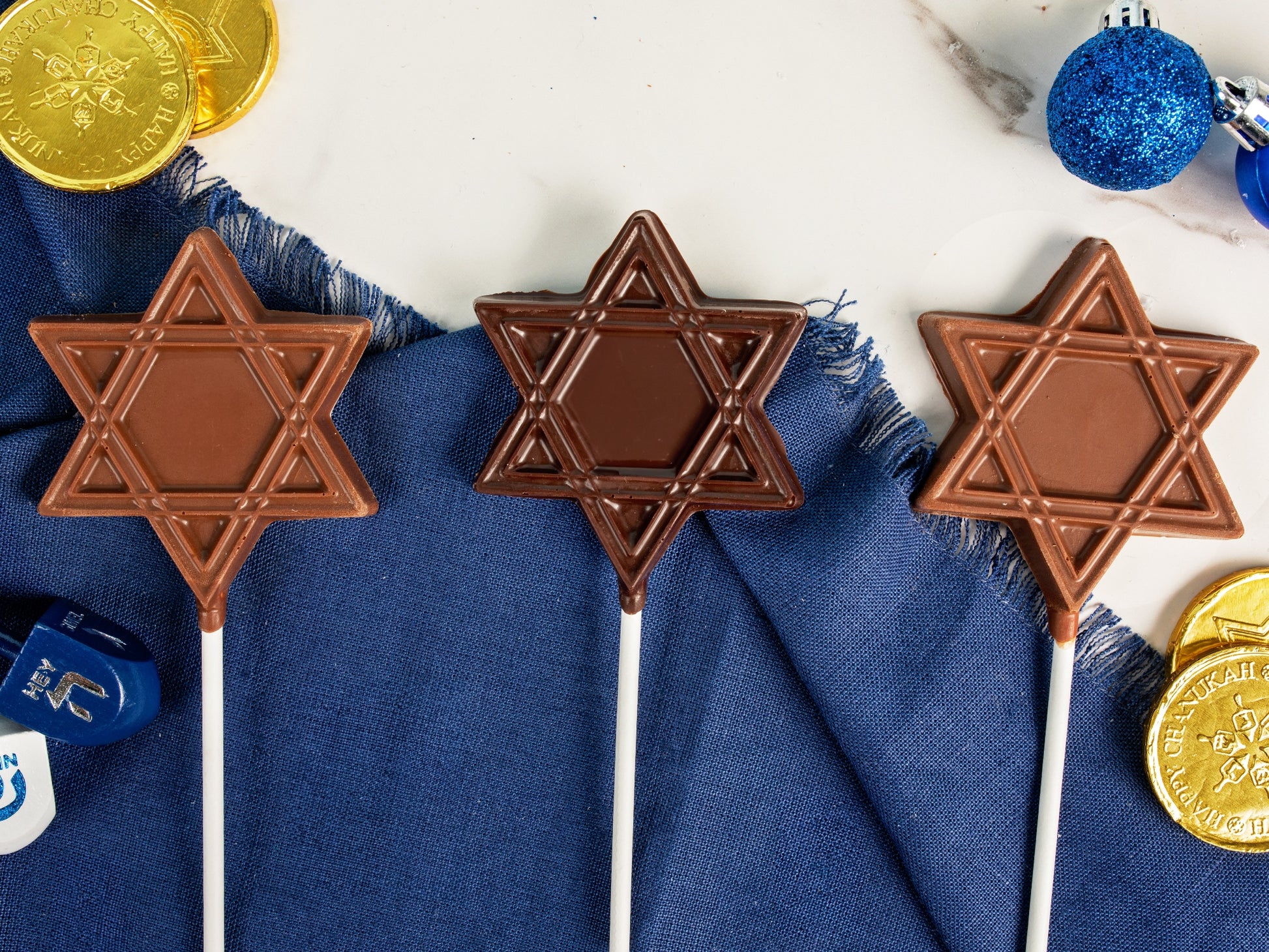 Three milk and dark star pops on a table with other Chanukah decorations.