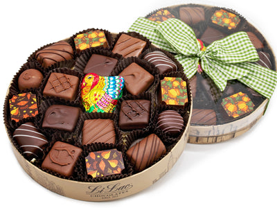 A round box with a clear lid is tied with a festive autumnal ribbon. The box contains 20 pieces of assorted chocolates including a foiled chocolate turkey.