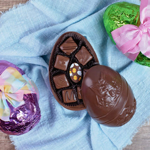 Large, chocolate egg mold, split in half, with 7 smaller chocolates inside. 2 other foiled eggs, one purple and one green