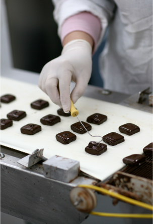 Bite sized dark chocolate squares on a white counter being made by Li-Lac staff