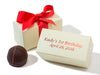 A gourmet chocolate ganache truffle sits next to two small square ivory cardstock boxes. One box is tied with a red ribbon bow. The other box shows an example of a printed message on the lid. The message says “Kady’s 1st Birthday April 28, 2016”.