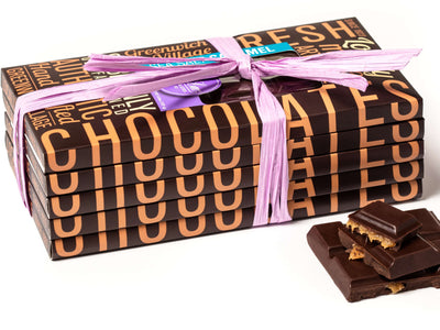 An assortment of our gourmet chooclate bars are stacked together and tied together with raffia. Some pieces of a bar are next to them, broken in half to reveal the filling inside.