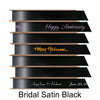 A stack of seven spools of shiny black satin ribbon with custom messages printed on them in different colors. 