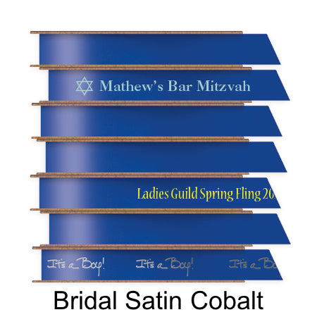 A stack of seven spools of shiny cobalt blue satin ribbon with custom messages printed on them in different colors. 