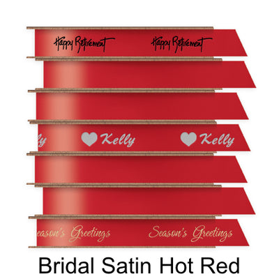 A stack of seven spools of shiny red satin ribbon with custom messages printed on them in different colors. 