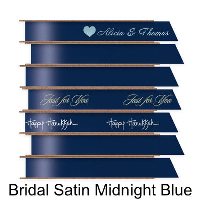 A stack of seven spools of shiny midnight blue satin ribbon with custom messages printed on them in different colors. 