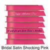 A stack of seven spools of shiny bright pink satin ribbon with custom messages printed on them in different colors. 
