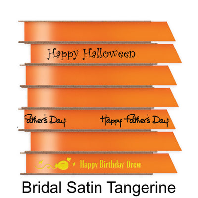 A stack of seven spools of shiny tangerine orange satin ribbon with custom messages printed on them in different colors. 