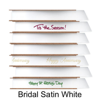 A stack of seven spools of shiny white satin ribbon with custom messages printed on them in different colors. 