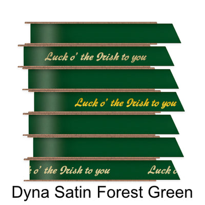 A stack of seven spools of shiny forest green satin ribbon with custom messages printed on them in different colors. 