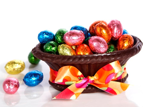 A basket made from molded chocolate holds chocolate eggs that are wrapped in brightly colored foil. 