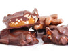 Pecan chews enrobed in milk or dark chocolate are stacked together. One is cut in half revealing the interior of a big dollop of caramel studded with pecans.