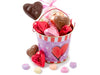 A little tin pail decorated with valentine's hearts is filled with some pieces of foil wrapped chocolate, conversation hearts and chocolate pops.