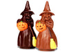 A big molded chocolate witch carries a jack-o-lantern friend and a broom stick. She wears a tall pointed witch's hat.