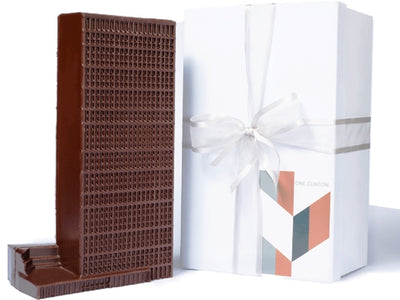 A sleek modern chocolate molded building next to a fancy whhite gift box tied with a ribbon.