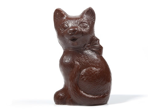 A cat molded out of chocolate sits. It has textured fur and a bow tied around its neck.