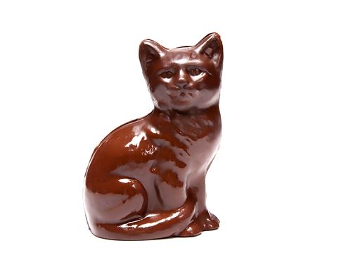 A cat molded out of chocolate sits with its little tail wrapped around its front leg. 