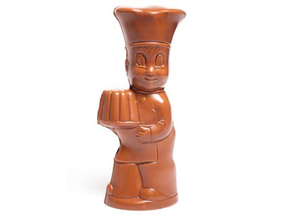 A molded chocolate Chef has a tall toque hat and holds a cake on a platter.