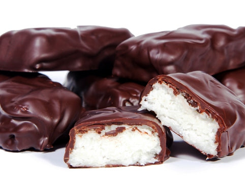 Bars of dark chocolate covered coconut are stacked up together. One bar is cut in half revealing the soft, moist coconut interior.