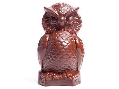 A molded chocolate Owl sits on a log. It has lots of detailed feathers.