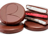 Flat, round disks of mint and raspberry soft cream are enrobed in dark chocolate. Several of the patties have been broken in half, reveling white mint cream centers and pink raspberry cream centers. 