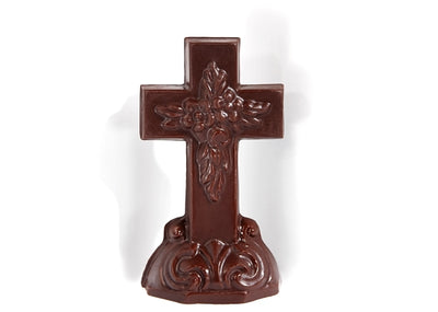 A molded chocolate Christian cross with a bouquet embossed at the intersection sitting upright in a molded chocolate base.