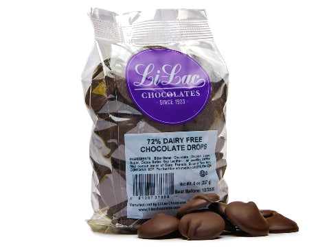 A clear cellophane bag of 72% Dark Dairy-Free chocolate drops sits with a few chocolate drops scattered on the table next to it. 