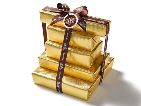 Five boxes of chocolate have been beautifully gift wrapped in gold foil paper. They are stacked on top of each other and tied together with a dark brown Li-Lac Chocolates logo printed ribbon with a round gift tag.