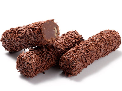 Little cylindrical rolls of chocolate ganache are lined up together. They are covered in chocolate sprinkles. One log is cut in half revealing the walnut studded, soft ganache interior.
