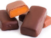 Thick caramel bars enrobed in milk and dark chocolate are stacked up together. The top bar is cut in half, revealing the soft, gooey caramel inside.