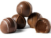 An assortment of gourmet truffles sit together. One truffle has a bite taken out of it, revealing the soft ganache center.