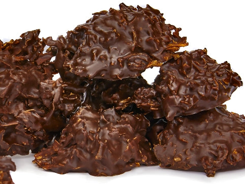 Mounds of toasted coconut enrobed in 72% dark dairy free dark chocolate are stacked up together.