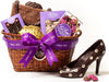 A wicker basket is filled with molded fashion chocolates as well as some other treats. The basket has a big purple Li-Lac Chocolates ribbon bow.