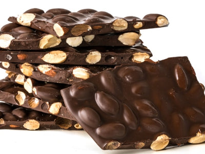 A stack of sugar free dark chocolate almond bark. The thin sheets of bark are broken into pieces, exposing the toasted almonds inside.