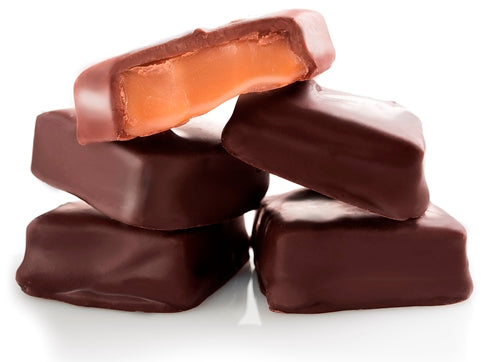 Caramel squares enrobed in milk and dark chocolate are stacked up together. The top square has a bite taken from it revealing the soft, gooey caramel inside.