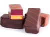 Thick rectangular bars enrobed in dark chocolate are stacked together. The bars have diagonal stripes piped in chocolate on the tops. One bar is cut in half revealing the layers of jellied raspberry and creamy peanut butter inside.