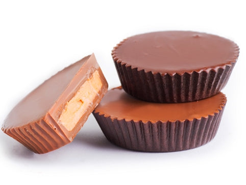 Milk and dark chocolate peanut butter cups are stacked together. One has been cut in half to reveal the creamy peanut butter center sandwiched between the top and bottom of chocolate in the cup.